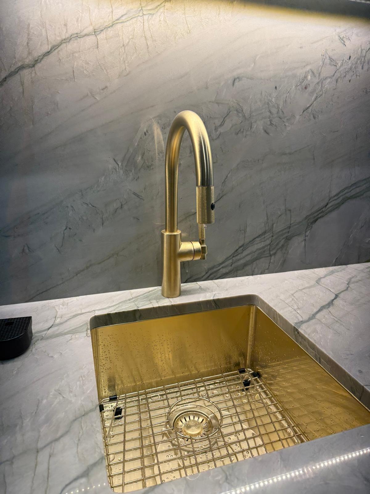 Kitchen sink with a brushed gold gooseneck faucet on marble