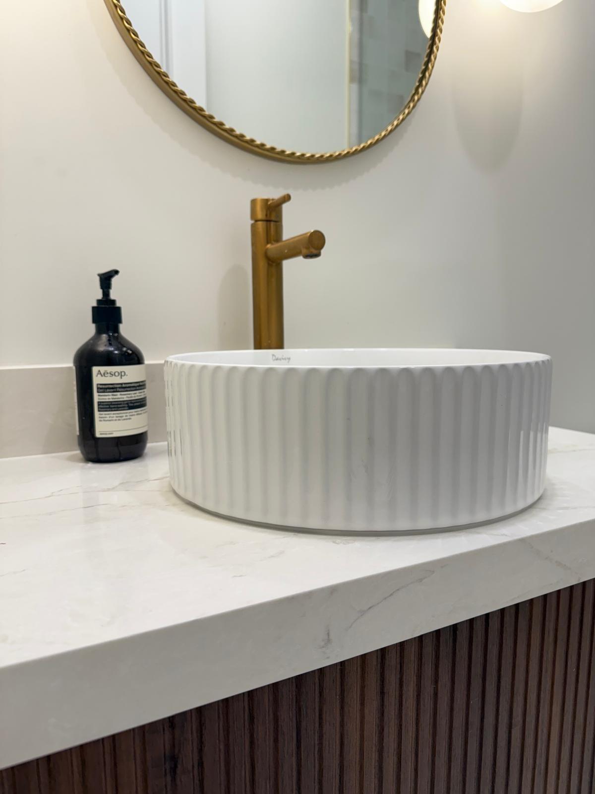 Fluted vessel sink with a brushed gold faucet on marble